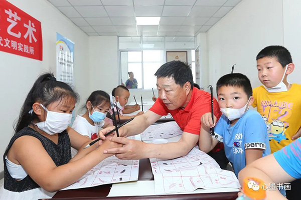 刘洪洋在活动现场手把手教授村中爱好书法的孩子书写规范姿势.jpg